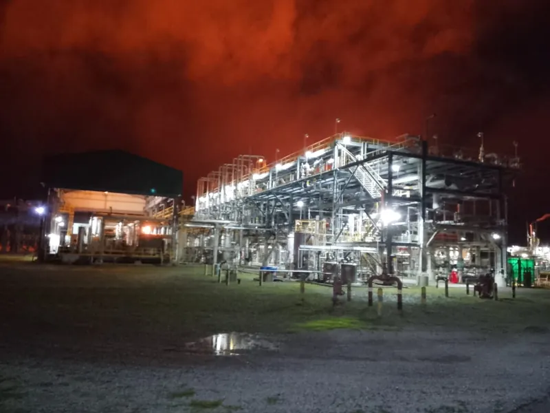 Planta industrial iluminada de noche, vista general de las estructuras y tuberías