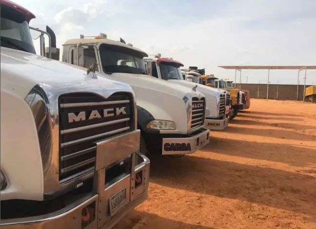 Fila de camiones Mack blancos estacionados en un patio de tierra