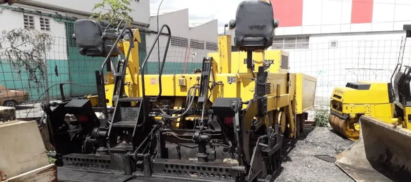 Pavimentadora de asfalto amarilla y rodillo compactador en un patio de maquinaria