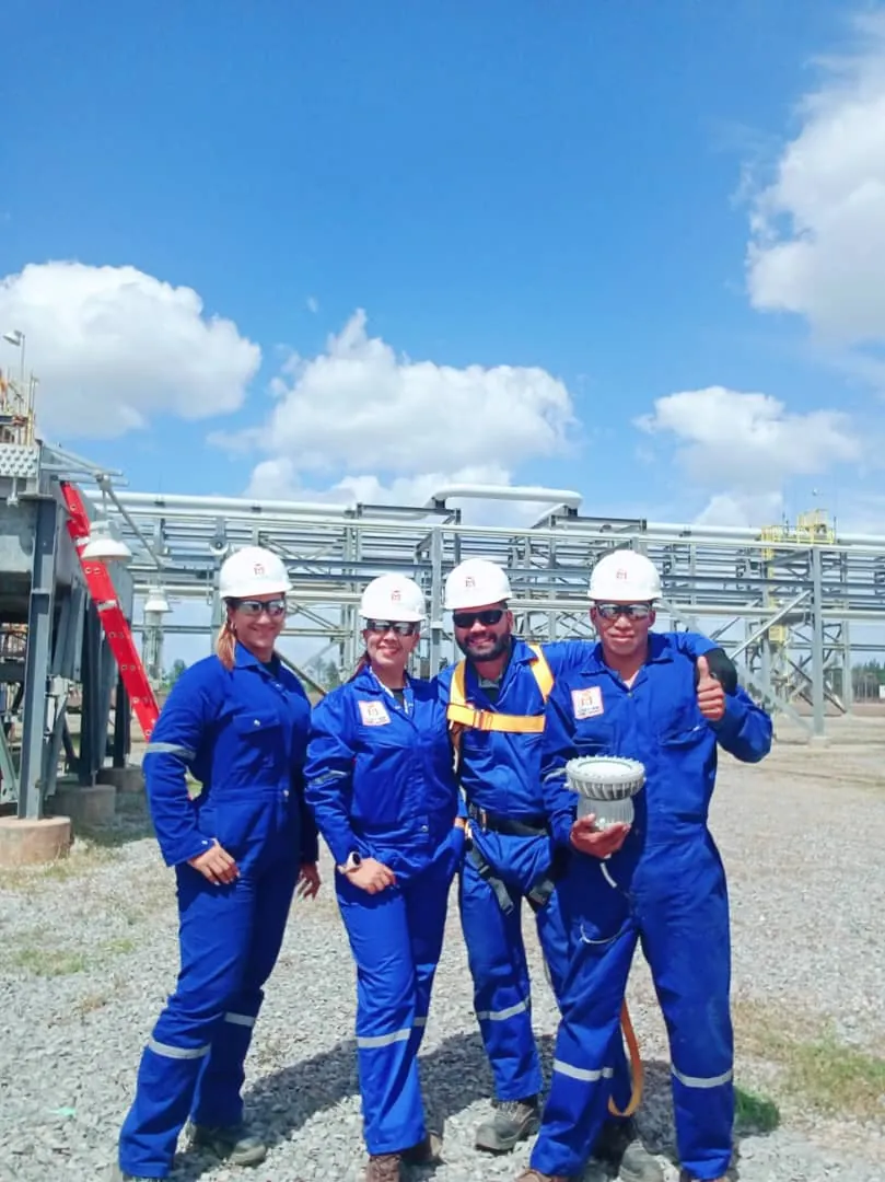Cuatro personas con braga azul y casco blanco en una instalación industrial; una sostiene una luminaria